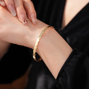 Close-up of a minimalist gold wavy geometric bracelet on a model with a black background