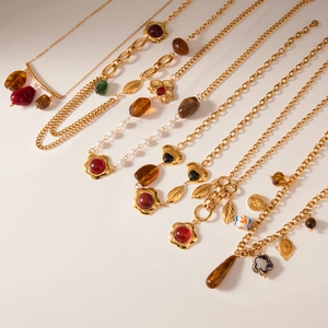 French vintage style gold necklaces with resin gemstones and pearls on beige background