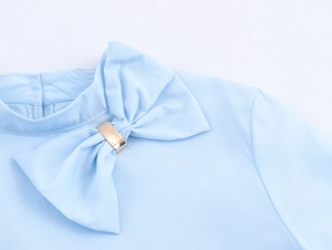 Detail of light blue blouse featuring a stand collar with a bow and gold metal buckle