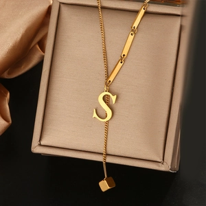 Gedetailleerd beeld van een gouden Y-vormige ketting met een S-letterhanger en kwastje