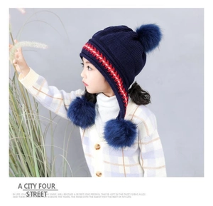 Dettaglio cappello in maglia blu con tre pompon e paraorecchie per bambini piccoli