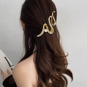 Elegant gold snake-shaped metal hair claw clip with pearl detail on a female model