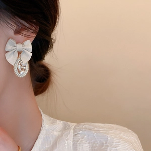 Close-up of elegant beige fabric bow earrings with pearl and crystal oval pendants