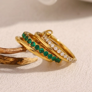 Detail of four-piece 18K gold-plated rings set with green and white zircons on wooden branch