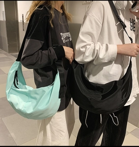 Outdoor lifestyle shot of models wearing light blue and black nylon crescent crossbody bags