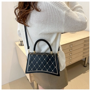 Close-up of black quilted shoulder bag with woven handle on a model in white sweater