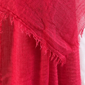 Detailed close-up of red cotton linen scarf texture featuring frayed raw edges