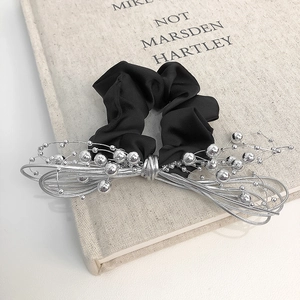 Minimalist silver bead chain hair tie with bowknot detail on a cream book background