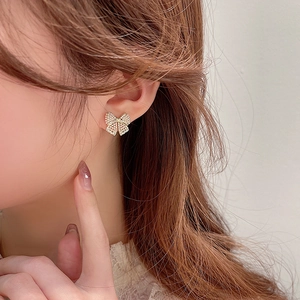 Close-up of golden bow-shaped stud earrings with micro pearls worn by a model