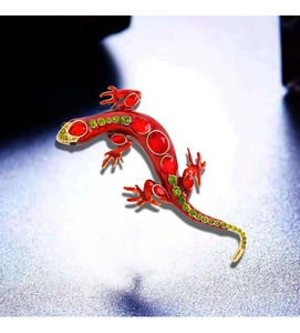 Detailed close-up of a lizard brooch with red enamel and green crystals on golden base