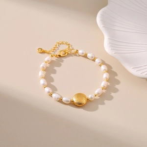 Macro detail of oval freshwater pearl bracelet with golden brushed metal charm and clasp