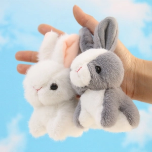 Close-up of white and grey plush rabbit keychains held against a blue sky background
