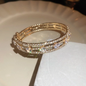 Macro shot of three-layer gold bracelet with sparkling cubic zirconia on white velvet