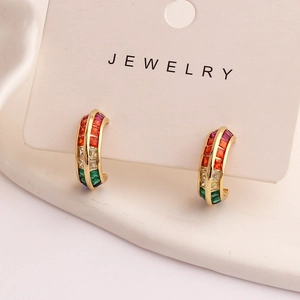 Detailed shot of gold C-shaped earrings with colorful square zircon on white stand