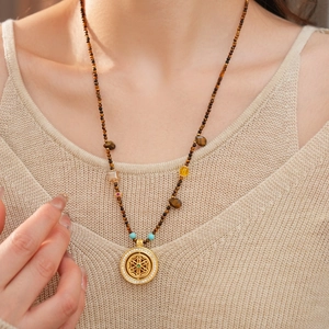 Tiger eye beaded long necklace with hollow gold pendant worn on beige sweater
