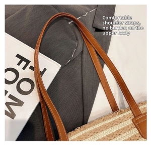 Close-up of woven straw tote bag with brown leather strap and contrast stitching detail