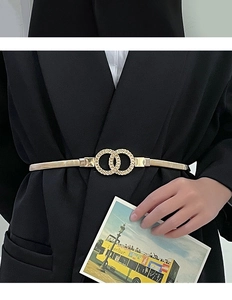 Close-up of gold interlocking circle buckle on a slim elastic metal belt and black blazer