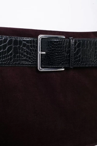 Détail d'une ceinture noire en croco avec boucle argentée sur du velours bordeaux