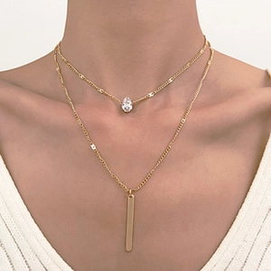 Close-up of gold layered necklace with teardrop zirconia and bar pendants on model