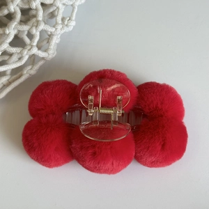 Detail showing red plush ball hair claw clip with transparent plastic clamp on white background