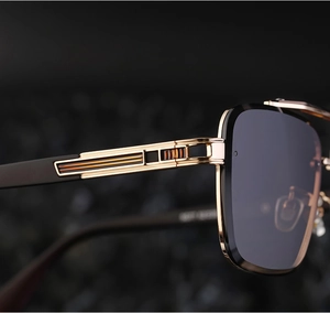 Macro shot of gold metal hinge details and textured temple on black square sunglasses