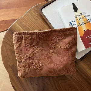 Close-up of floral embroidery on a vintage camel suede cosmetic bag on wooden table