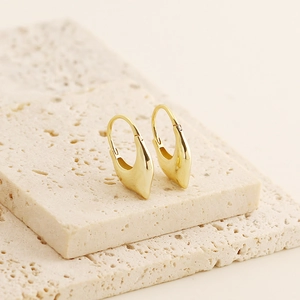 Detailed view of polished gold teardrop earrings resting on natural stone texture
