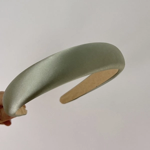Detail of light green satin sponge headband with beige lining held against white background