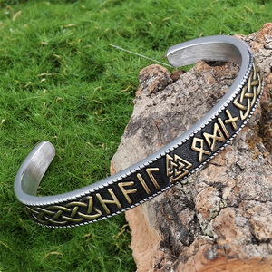 Detail of Viking cuff bracelet with gold Celtic knots and runes on mossy wood base
