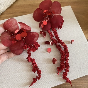 Detail of red fabric flower earrings with sequins and long wavy tassels on linen