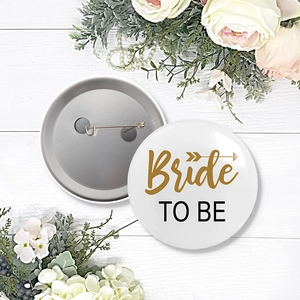 Detail of Bride to be tinplate badge with safety pin back on white wood and floral background