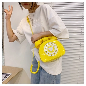 Creative yellow retro rotary phone crossbody bag in shiny patent leather on a model
