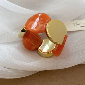 Détail macro du bracelet élastique avec résine marbrée orange et blocs de métal doré