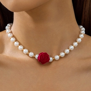 Detailed view of a pearl necklace with a red velvet rose pendant on a model's neck