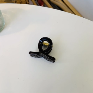 Top view of a glossy black minimalist twist hair claw clip with a gold metal spring