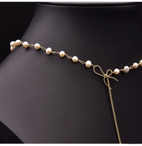 Detail of white pearls with a golden bow pendant on a long metallic sweater chain