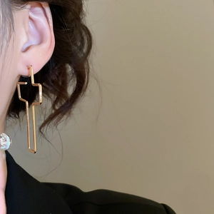 Gros plan d'une boucle d'oreille dorée géométrique croisée portée de profil