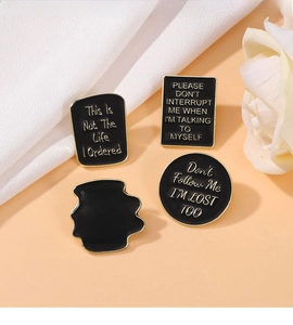 Macro shot of four black enamel pins with gold trim and humorous text on orange backdrop