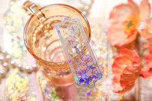 Close-up of laser floral PVC bookmark with golden relief on an amber glass cup