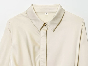 Détail du col d'une chemise en satin avec bouton doré et texture de soie ivoire lisse