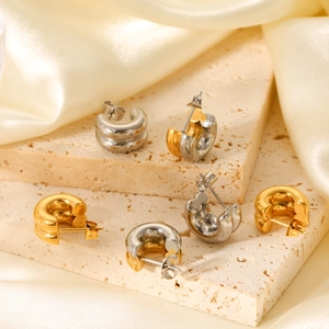 Chunky C-shaped 18K gold and silver stainless steel earrings on beige travertine stone