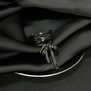 Detailed close-up of dark metal bow-shaped ring on black silk with zircon accents