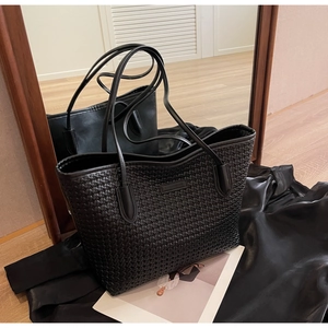 Close-up of black woven leather tote bag resting on magazines in a stylish home setting