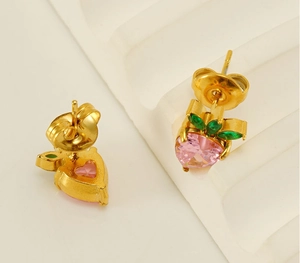 Macro view of gold strawberry stud earrings with pink heart crystals and green gems