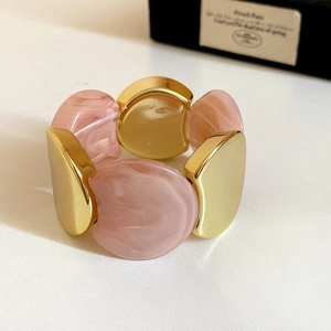 Close-up of pink marble resin and polished gold metal segments on a wide bracelet