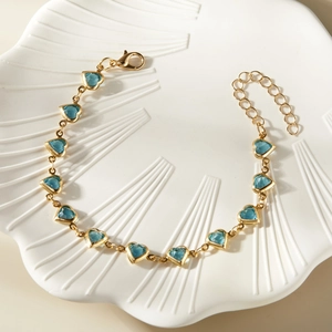 Detail of golden bracelet featuring vibrant blue heart charms and lobster clasp closure
