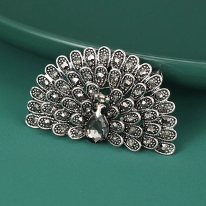 Detailed view of vintage silver peacock brooch with grey rhinestones on dark green ceramic