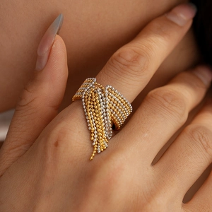 Makroaufnahme eines gold-silbernen Perlen-Quastenrings am Finger mit Metalltextur