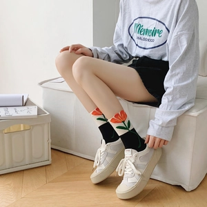 Detail of women's black crew socks featuring red tulip embroidery on beige ribbed cuffs
