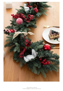 Detail of Christmas garland with pine cones, red berries and plaid bows on wooden table